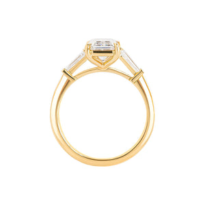 Yellow gold engagement ring set with an emerald cut lab diamond and tapered baguette sides. Cathedral set. Gallery view.