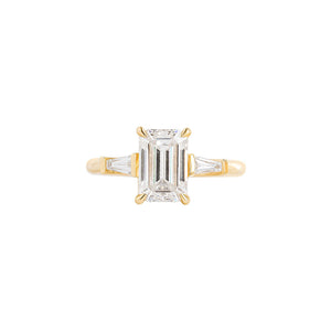 Yellow gold engagement ring set with an emerald cut lab diamond and tapered baguette sides. Cathedral set. Front view