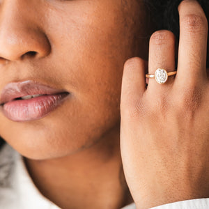 Portrait of a woman wearing an oval bezel-set solitaire moissanite engagement ring in yellow gold.