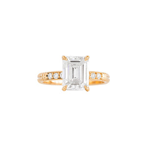Yellow gold moissanite or lab diamond emerald cut engagement ring with lab diamond pave and antique engraving on a white background. Peg head setting. Front view.