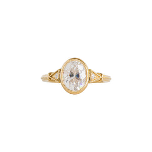 Yellow gold bezel-set antique-inspired oval engagement ring on a white background. Ring has hand-carved milgrain on the bezel and side triangles with accent lab diamonds. Integrated basket, antique fluting on shank. Front view.