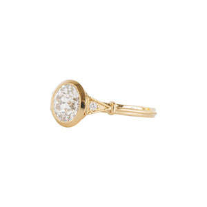 Yellow gold bezel-set antique-inspired Old European Cut round engagement ring on a white background. Ring has hand-carved milgrain on the bezel and side triangles with accent lab diamonds. Integrated basket, antique fluting on shank. Side view.