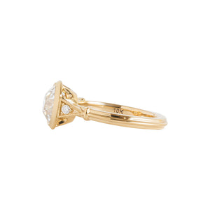 Yellow gold bezel-set antique-inspired Old European Cut round engagement ring on a white background. Ring has hand-carved milgrain on the bezel and side triangles with accent lab diamonds. Integrated basket, antique fluting on shank. Side view.