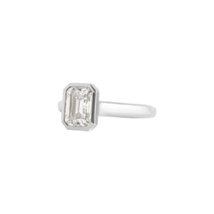 White gold bezel-set emerald cut moissanite or lab diamond solitaire engagement ring on a white background. Floating gallery cathedral. Side view.