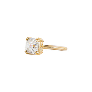 Double claw prong yellow gold Asscher cut moissanite or lab diamond solitaire engagement ring on a white background. Knife edge band with an integrated basket. Side view.