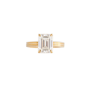 Yellow gold emerald moissanite or lab diamond engagement ring on a grooved band with ridges, on a white background. Integrated basket. Front view. 