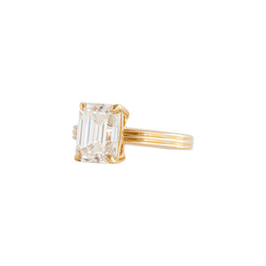 Yellow gold emerald cut moissanite or lab diamond engagement ring on a grooved band with ridges, on a white background. Cathedral setting. Side view. 
