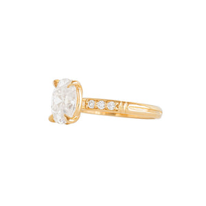 Yellow gold moissanite or lab diamond oval cut engagement ring with lab diamond pave and antique engraving on a white background. Peg head setting. Side view.