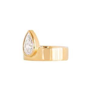 Asymmetrical yellow gold engagement ring on a white background. Pear moissanite or lab diamond offset onto a wide band. Side view. 