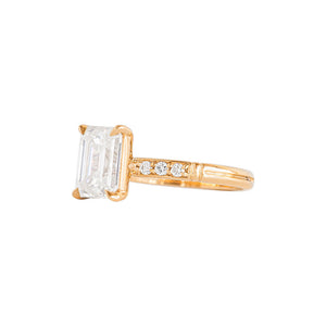 Yellow gold moissanite or lab diamond emerald cut engagement ring with lab diamond pave and antique engraving on a white background. Peg head setting. Side view.