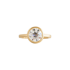Yellow gold bezel-set engagement ring with hand-carved milgrain and integrated basket, on a white background. Set with an Old European Cut round moissanite or lab diamond. Front view.
