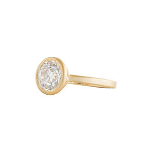 Yellow gold bezel-set engagement ring with hand-carved milgrain and integrated basket, on a white background. Set with an Old European Cut round moissanite or lab diamond. Side view.
