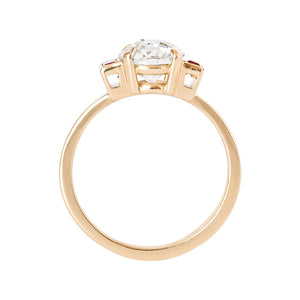 Yellow gold engagement ring with four claw prongs and vertical lab grown ruby baguettes, set with an Old European Cut moissanite or lab diamond. Gallery view.