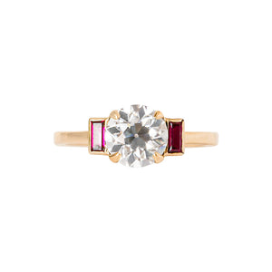 Yellow gold engagement ring with four claw prongs and vertical lab grown ruby baguettes, set with an Old European Cut moissanite or lab diamond. 