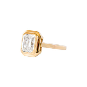 Yellow gold emerald cut moissanite or lab diamond engagement ring with a wide stepped bezel setting and an integrated basket on a white background. Side view.