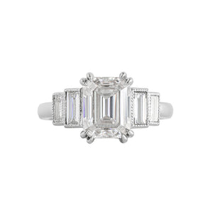 White gold emerald cut moissanite or lab diamond engagement ring with four vertical lab diamond baguette accent stones, on a white background. Center stone has double prongs, baguettes are bezel-set with hand-carved milgrain on the bezel. Front view.