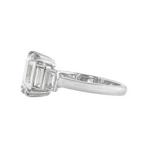 White gold emerald cut moissanite or lab diamond engagement ring with four vertical lab diamond baguette accent stones, on a white background. Center stone has double prongs, baguettes are bezel-set with hand-carved milgrain on the bezel. Side view.