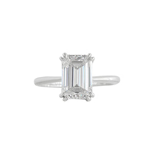 Double claw prong white gold emerald cut moissanite or lab diamond solitaire engagement ring on a white background. Knife edge band with an integrated basket. Front view.