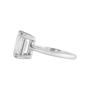 Double claw prong white gold emerald cut moissanite or lab diamond solitaire engagement ring on a white background. Knife edge band with an integrated basket. Side view.