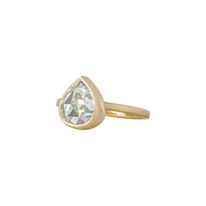 Yellow gold bezel-set engagement ring with hand-carved milgrain and integrated basket, on a white background. Set with a rose cut chubby pear moissanite or lab diamond. Side view. 
