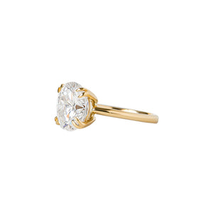  Double claw prong yellow gold oval cut moissanite or lab diamond solitaire engagement ring on a white background. Knife edge band with an integrated basket. Side view.