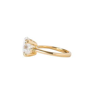  Double claw prong yellow gold oval cut moissanite or lab diamond solitaire engagement ring on a white background. Knife edge band with an integrated basket. Side view.