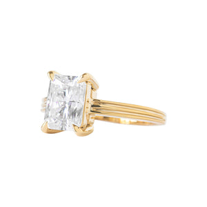 Yellow gold radiant moissanite or lab diamond engagement ring on a grooved band with ridges, on a white background. Integrated basket. Side view. 