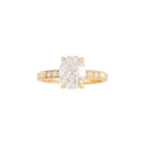Yellow gold moissanite or lab diamond oval cut engagement ring with lab diamond pave and antique engraving on a white background. Peg head setting. Front view.