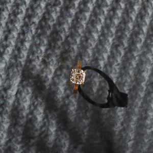 Yellow gold Asscher moissanite or lab diamond engagement ring on a grooved band with ridges, on a textured black background. Integrated basket. Front view. 