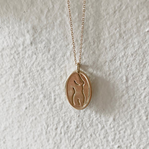 Gold oval pendant engraved with a nude female line drawing.
